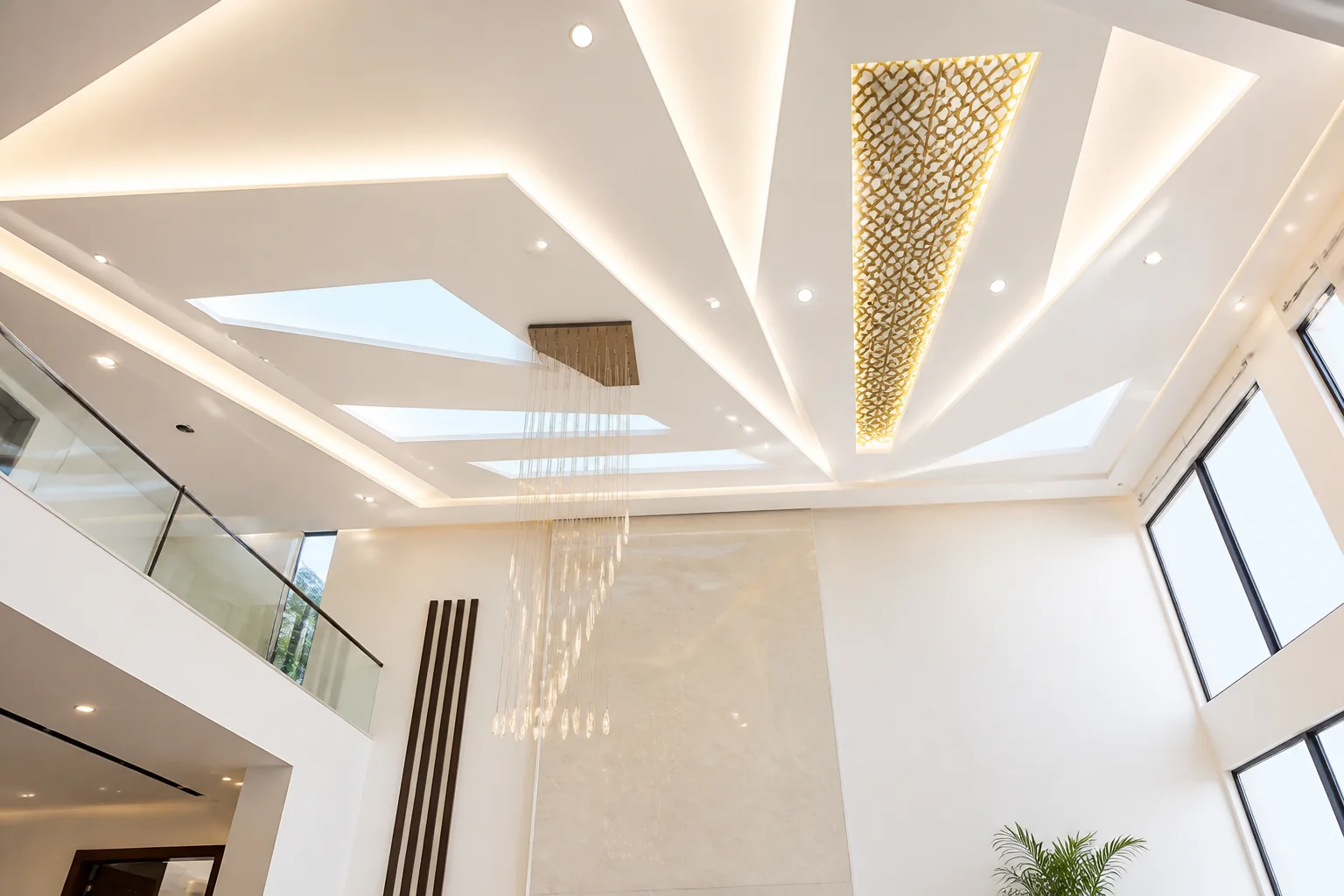 Double-height foyer false ceiling with cascading geometric recesses, cove lighting, and suspended sculptural luminaire